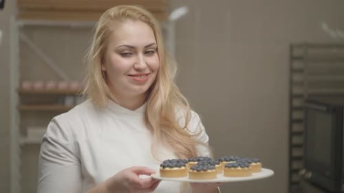 Smiling Chef Confectioner Woman Holding Her Bakery Tarts with Blueberries on Plate in Slow Motion