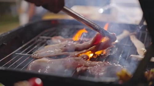 Nahaufnahme vom Grillen von Fleisch auf dem Grillrost, brennendes Feuer mit Rauch in dunkler Nacht im Camp.