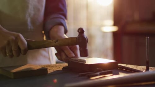 Nahaufnahme der Hände einer kaukasischen Juwelierin mit Hammer zur Schmuckherstellung