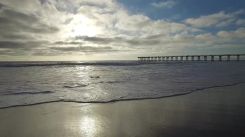 Tracking shot of the ocean waves, beach and pier at sunset.