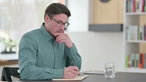 Man Writing in Notebook at Desk