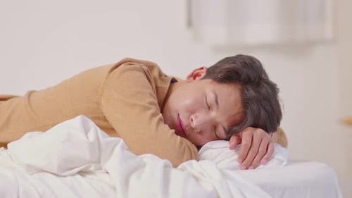 Beau et attrayant homme asiatique dort et fait de doux rêves allongé sur le lit dans une chambre confortable