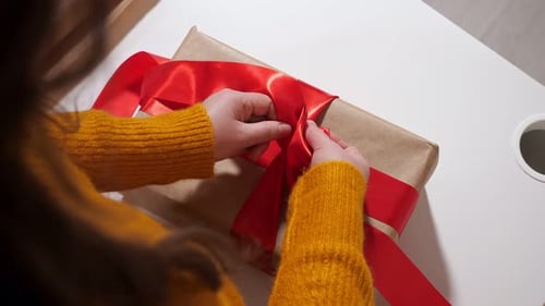 Unrecognizable Woman Ties a Gift Box with a Red Ribbon Top View