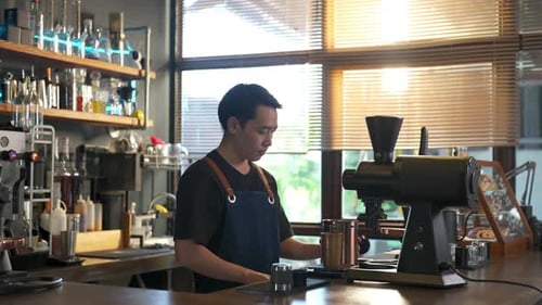 4K Barista aus Asien, der geröstete Kaffeebohnen in einer Kaffeemühle mahlt