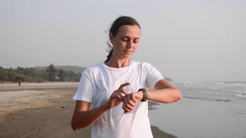 Frau joggt am Meeresstrand und benutzt den Fitnessuhr-Timer