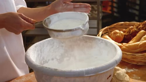 Baker Sifting Flour into Bowl at Workplace