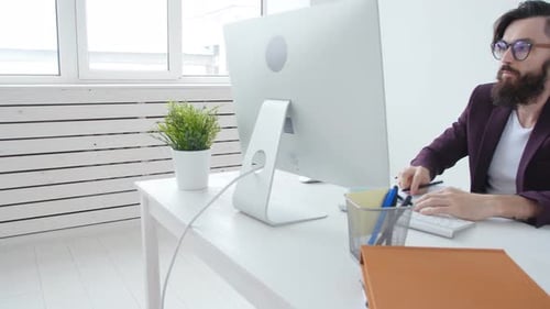 Concept de travail de bureau ou de pige. Jeune homme élégant barbu travaillant à l'ordinateur