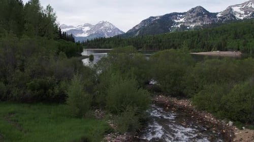 Rising aerial view over river revealing lake and mountains.
