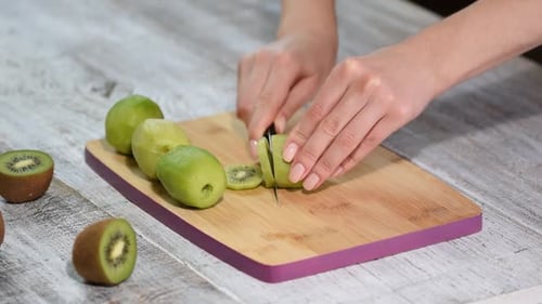 Hand slicing a kiwi with a knife, close up