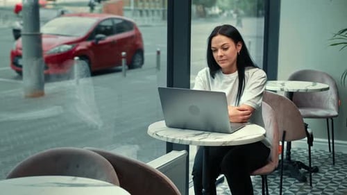 A beautiful woman works on a laptop, leads a zoom call in a cafe. Freelancer, businessman.