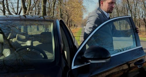 Young Businessman Driver Gets Out of Car and Looks on Breakdown Automobile on the Road