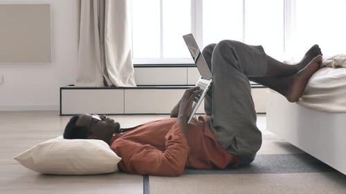 Lazy AfricanAmerican Man Works on Laptop Lying on Floor