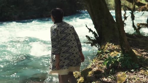 Glamouröse junge Frau geht im Wald über das Flussufer und setzt sich