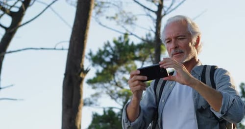 Senior Man Takes Pictures with Smartphone in Forest