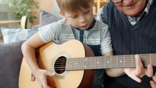 Elderly Man Teaching Grandson To Play the Guitar in Apartment Bonding