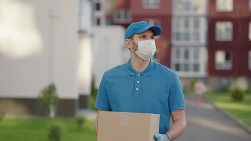 An Young Mailman Courier with a Protective Mask and Gloves is Delivering a Parcel Directly to a