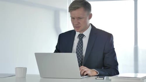 Frustrated Businessman Working on Laptop in Modern Office