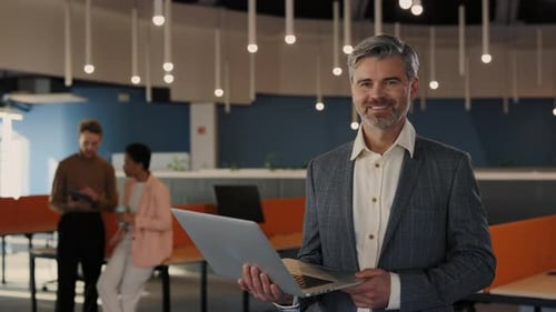 Portrait of Handsome Businessman Looking at the Camera Holding Laptop Standing in the Office