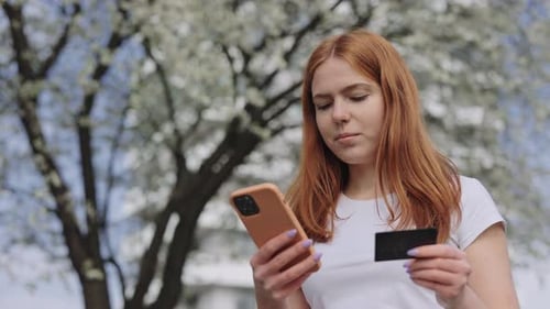 Redhead Woman Using Mobile and Credit Card in Spring Park