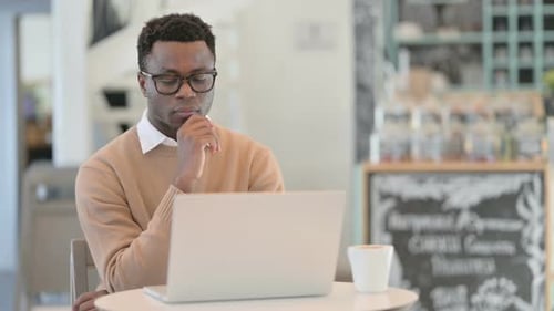 Creative African Man Thinking While Using Laptop in Cafe