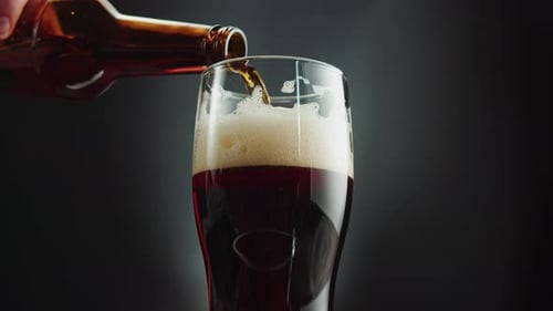 Dark Beer Pouring into Glass with Foam Head