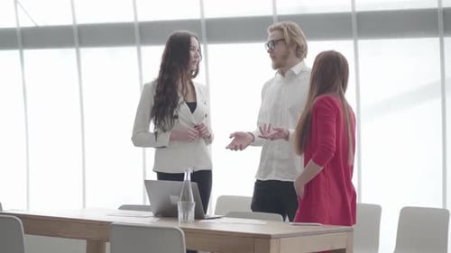 Geschäftsmann in Brille gestikuliert, während er zwei weiblichen Kollegen, die dabei stehen, seine Idee erklärt
