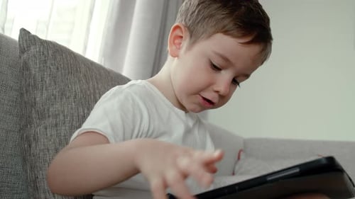 Boy Concentrating on Tablet Device While Indoors