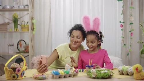 Mom and Daughter with Funny Bunny Ears Talk on a Video Call Using the Phone