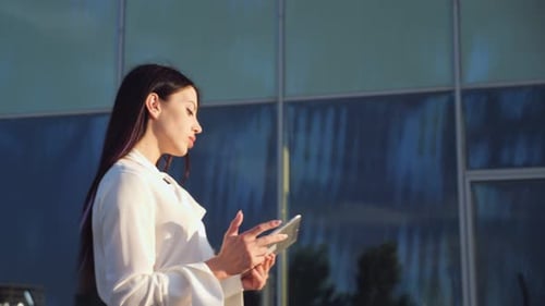 Lady Manager Walks Past Glass Office and Works in Tablet