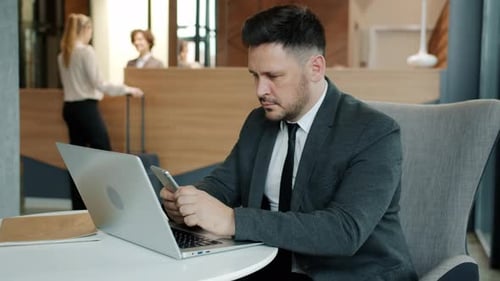 Cheerful Man in Suit Using Smartphone Texting Smiling Sitting in Hotel Lobby