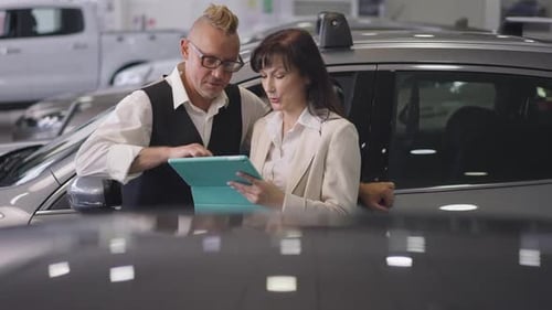 Un couple marié caucasien réussi examine les nouvelles caractéristiques du véhicule sur une tablette debout dans une voiture