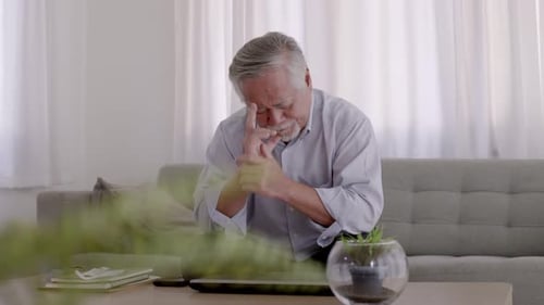 Senior Man Rubs Face on Couch in Home