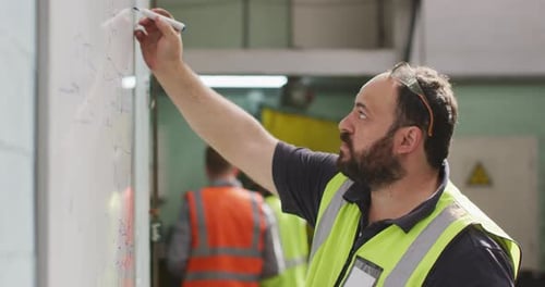 Caucasian male factory worker at a factory writing on white board