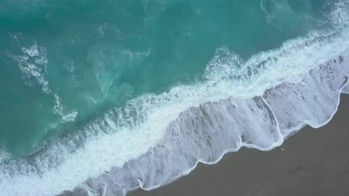 Aerial Top Down Turquoise Sea Waves Foaming and Splashing Reaching Shore From Above Empty Beach