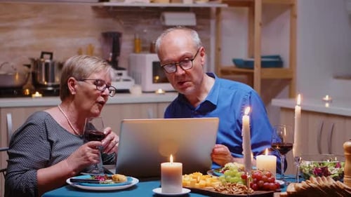 Elderly Couple Using Laptop at Dinner Table