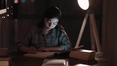 Focused Woman Writing at Desk Under Lamp at Night