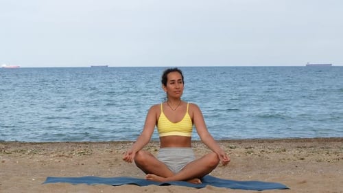 Beautiful tanned young woman sitting in a meditation pose on the beach. Goods for health.