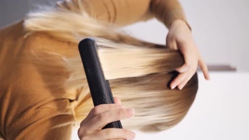 Woman Styles Blonde Hair With Hair Straightener