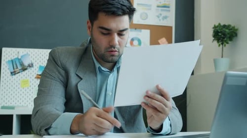 Ambitious Businessman Reading Papers and Taking Notes Concentrated on Business Development Working