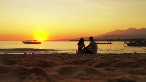 Romantic couple male and young woman silhouette sitting on the tropical beach enjoying sunset and oc