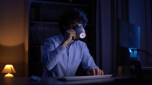 Trabajador autónomo cansado y con exceso de trabajo que trabaja en la computadora y bebe café de la taza sentado en