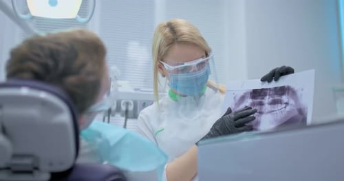 Dentist Shows the Patient an Xray of the Teeth and Tells How the Treatment Will Take Place