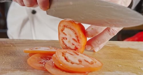 Slow motion close up of a chef knife slicing a tomato