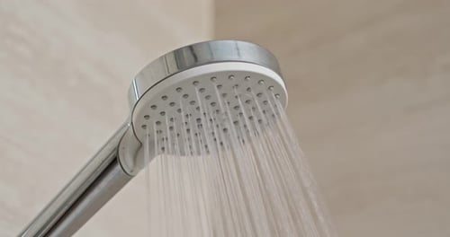 Water Flowing from Modern Shower Head in Bathroom