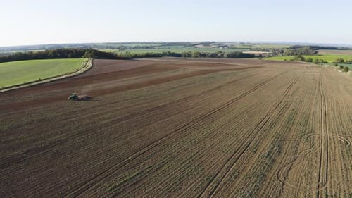Aerial Drone Shot a Field with a Tractor in a Rural Area on a Sunny Day Drone Flies Across Field