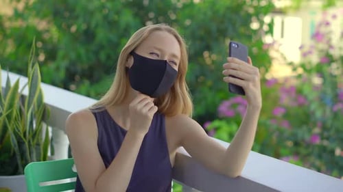 Blonde Woman Wearing Mask Using Phone on Balcony