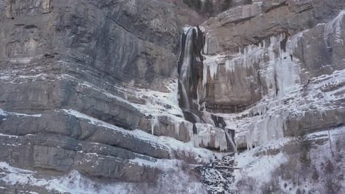 A half frozen half flowing waterfall flowing down rugged terrain in the Rocky Mountains