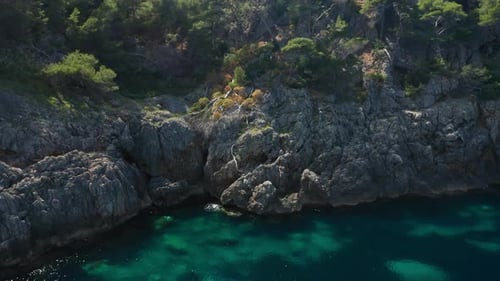 Drone Flight Along Sunlit Turquoise Sea And Rocky Coastline