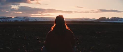 Homem se senta enquanto olha para o pôr do sol