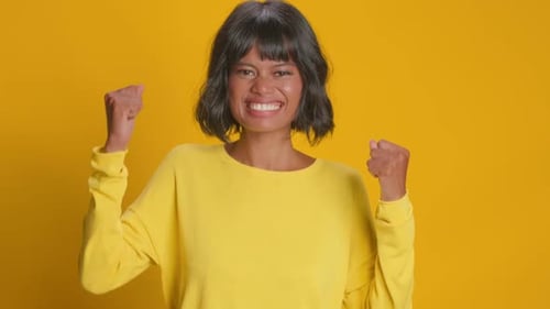 Excited Woman Celebrating Victory in Yellow Studio